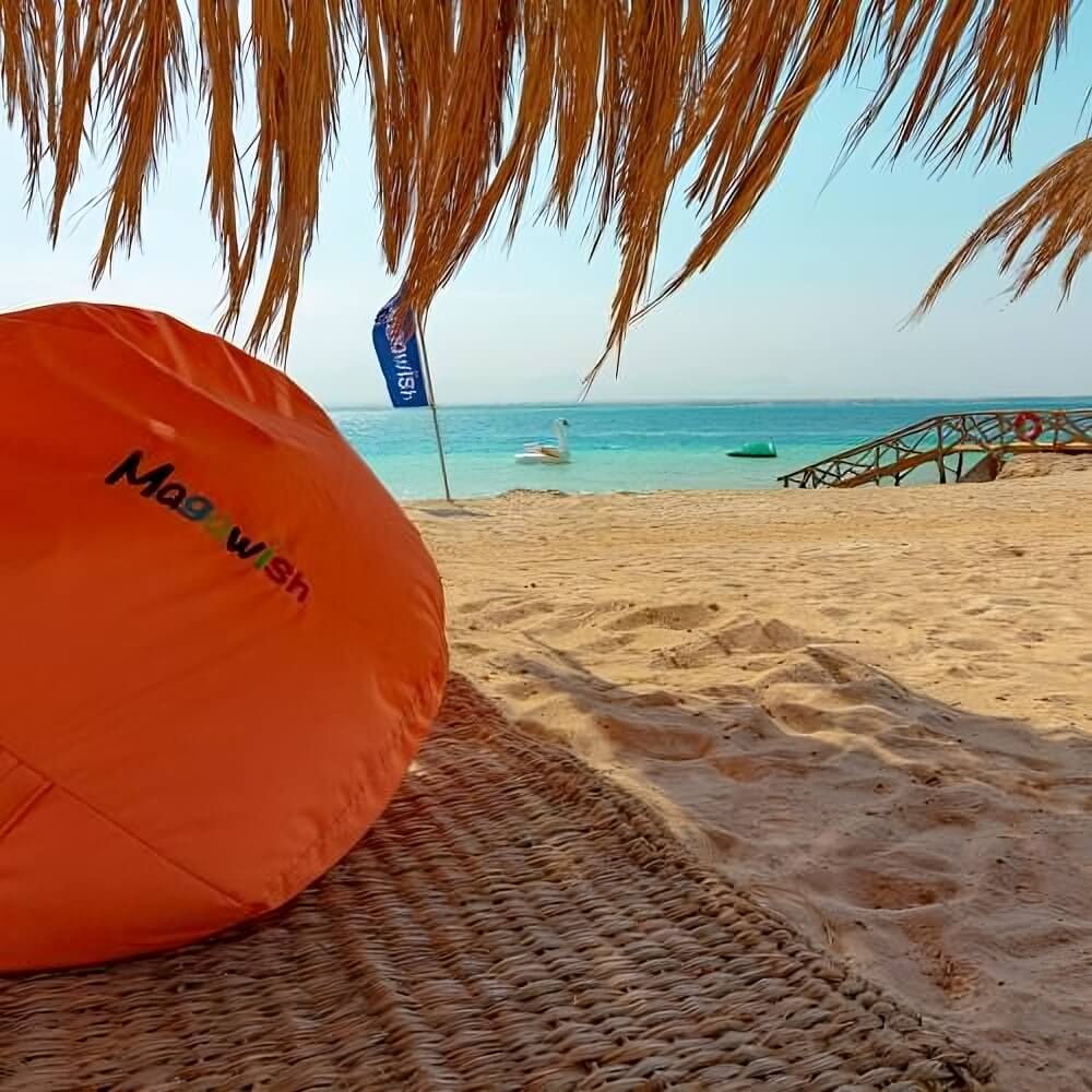 Relaxing beach view under palm canopy with orange bean bag and Red Sea backdrop – luxury island retreat near Hurghada, Egypt